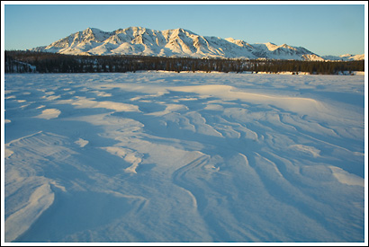 Windblown snow, sunset, over frozen Twin Lakes, and the mentasta Mountain Range, winter, Wrangell-St. Elias National Park, Alaska.