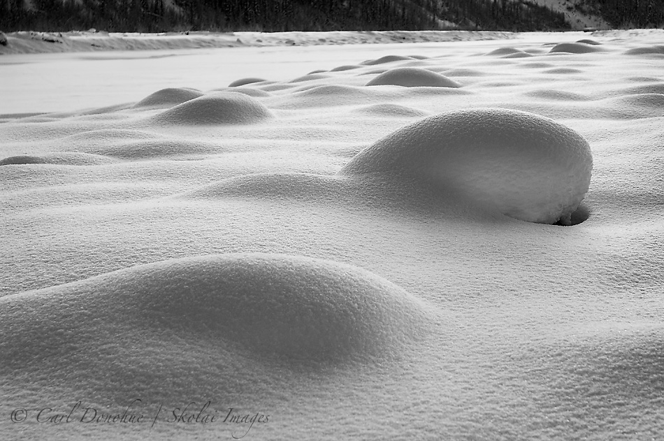 Snow covered boulders glisten in late evening sun. Winter light on fresh snow, along the frozen Kennicott River, or Kennecott River, Wrangell-St. Elias National Park and Preserve, Alaska.